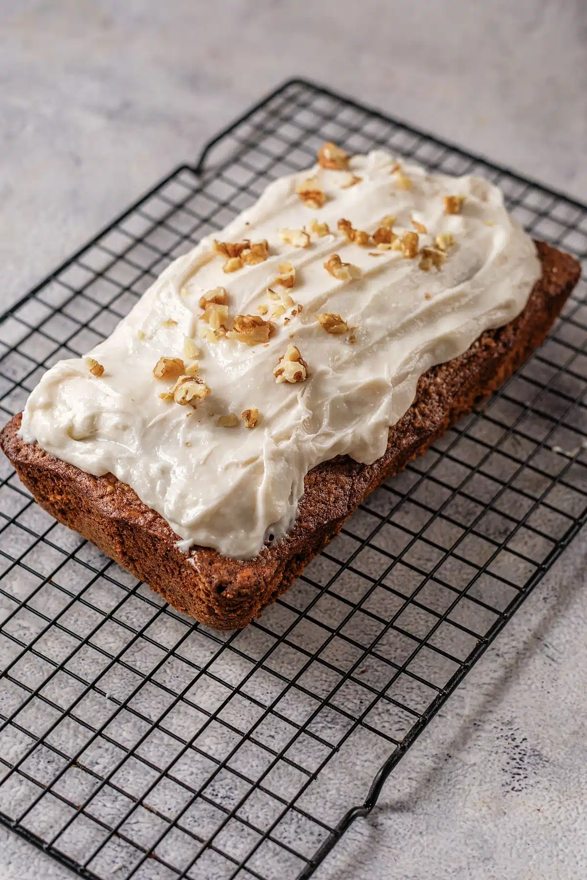 Gingerbread loaf on a wire rack under a thick layer of cream cheese frosting