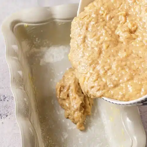 Thick pale batter poured from a bowl into a greased ceramic loaf pan
