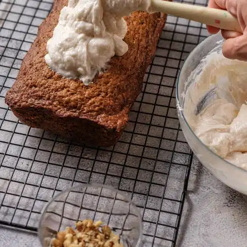 A spatula spreading white frosting over the top of the cooled cake
