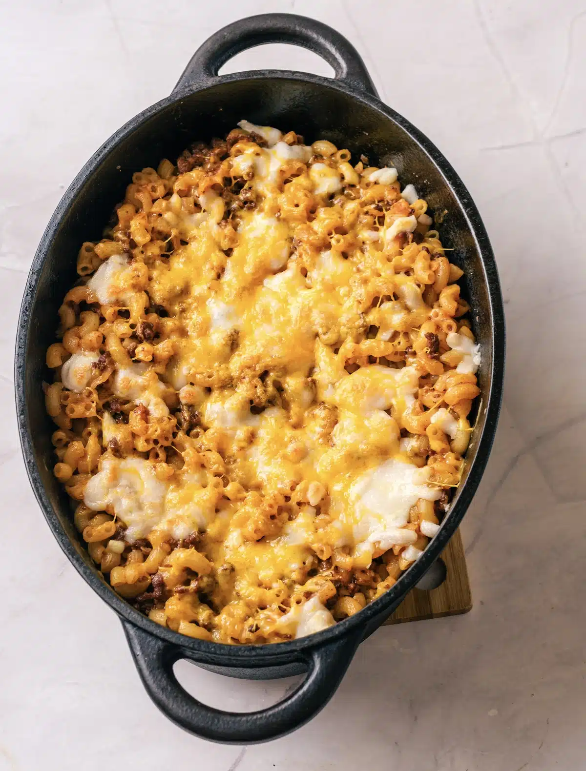 Homemade beefaroni in an oval cast-iron pot seen from above, with cheddar and mozzarella melted over the top
