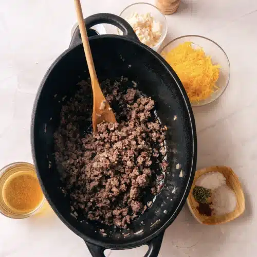 Ground beef browned and broken up in a black pot with a wooden spoon