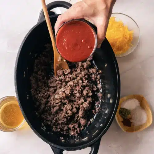 Tomato sauce poured from a bowl over the browned beef