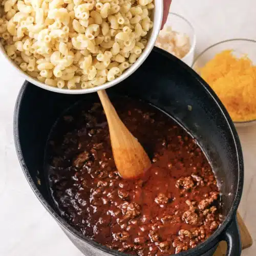 Cooked corkscrew pasta tipped from a bowl into the meat sauce