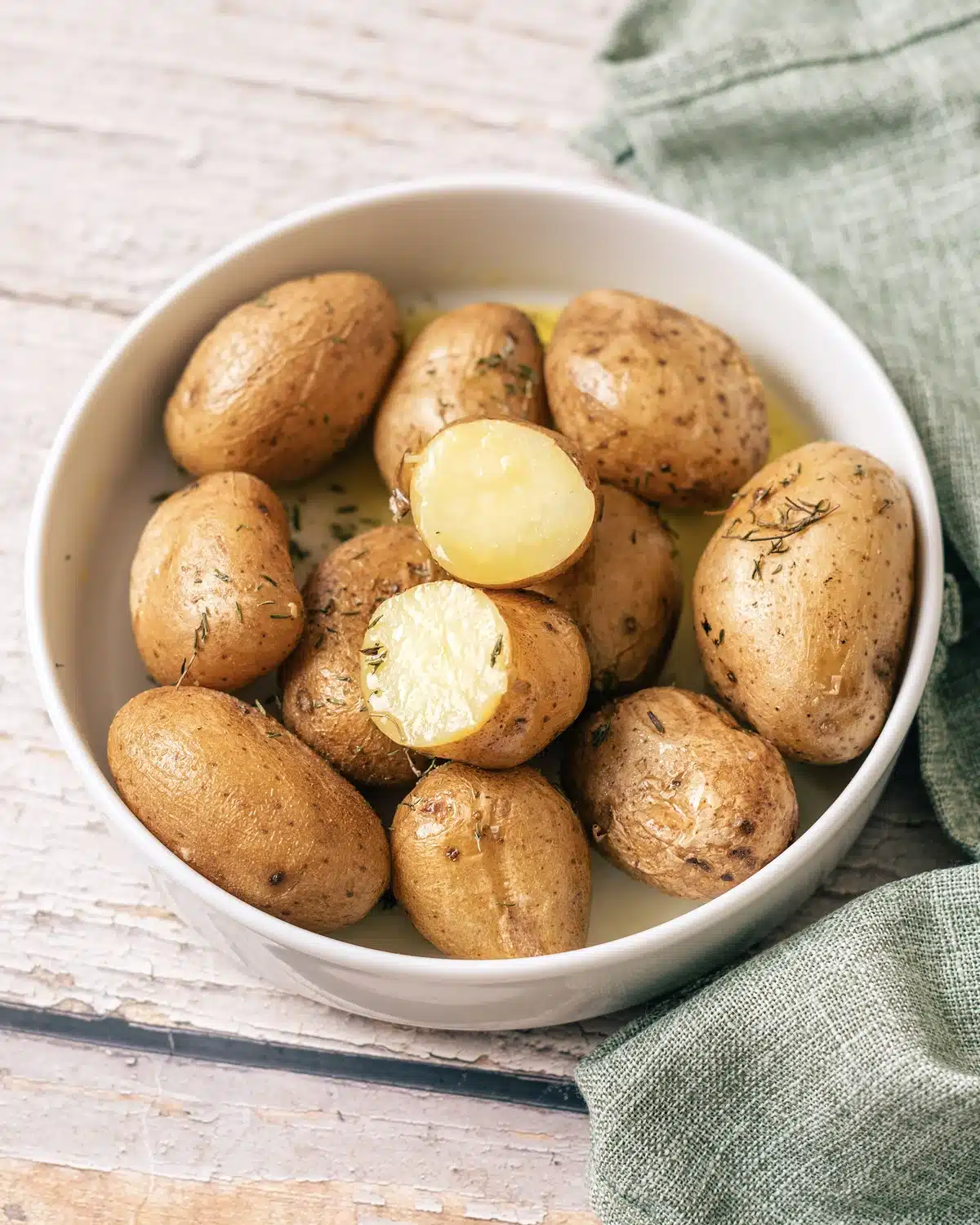 Syracuse salt potatoes in a white bowl with melted butter and thyme, one cut open to show the creamy inside