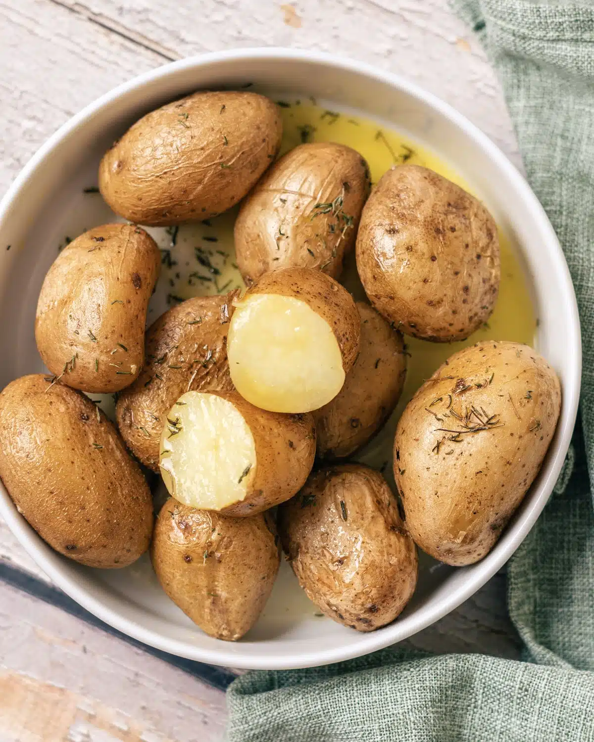 A close view of two halved spuds showing pale yellow, creamy flesh under wrinkled skin in a pool of butter
