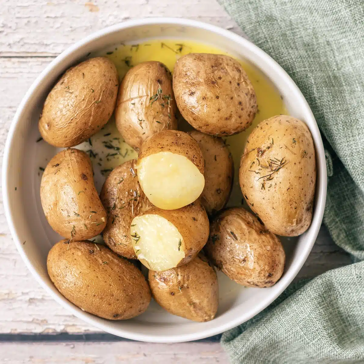 Salt potatoes seen from above in a shallow white bowl with butter pooled at the bottom
