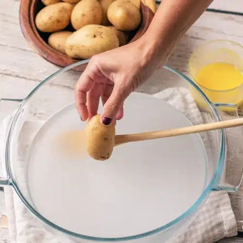 A small potato lowered on a wooden spoon into the cloudy brine