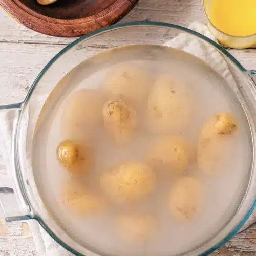 Small potatoes simmering in cloudy salted water in a glass dish