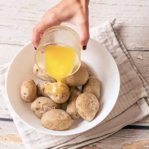 Melted butter poured from a glass over drained boiled potatoes in a white bowl