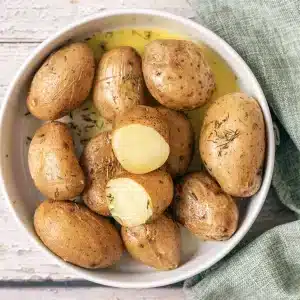 A bowl of salt potatoes with melted butter and thyme, two cut open