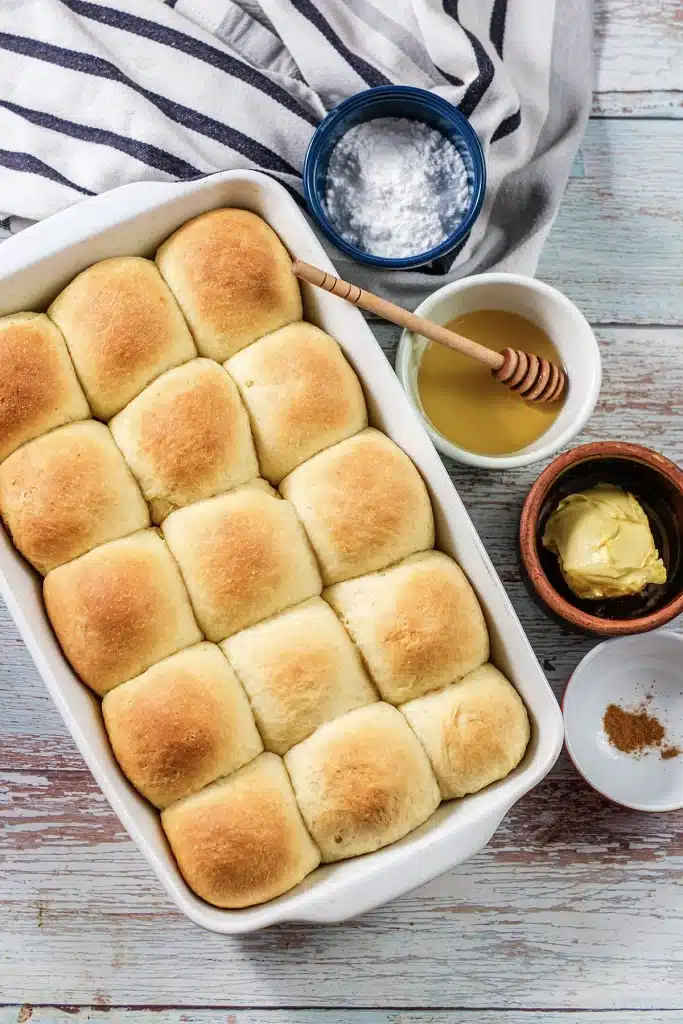 Texas Roadhouse rolls in a white baking dish with honey, butter and cinnamon alongside