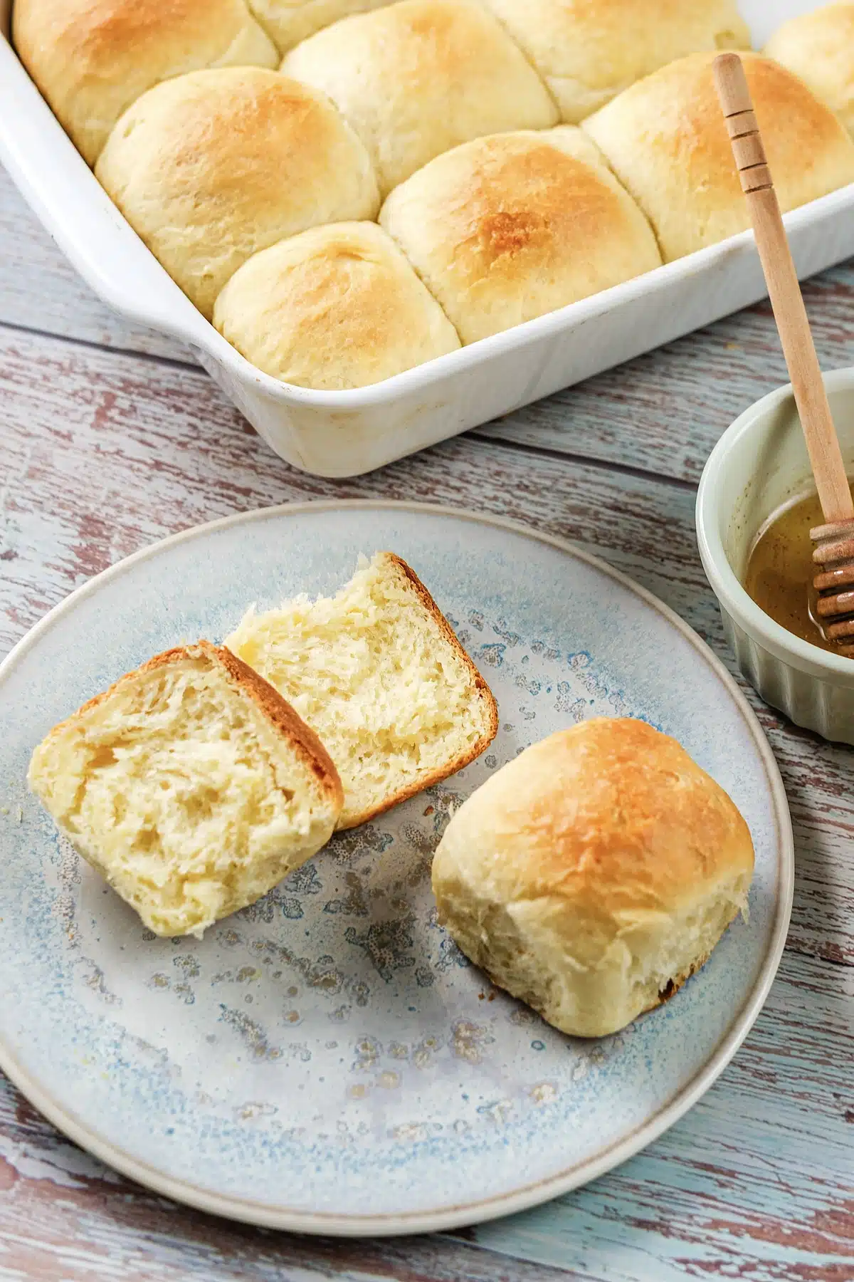 Texas Roadhouse rolls split open on a plate beside a small pot of honey