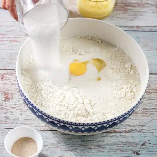 Sugar poured into a bowl of flour with an egg in the middle