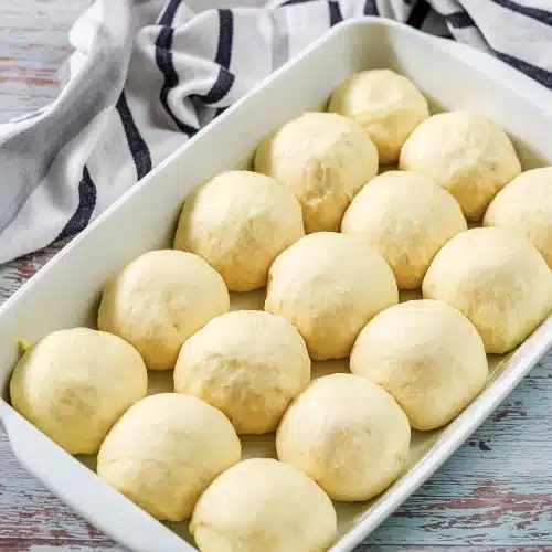 Twelve smooth dough balls risen in a buttered white dish