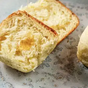 One halved dinner roll on a speckled plate with honey pooling in the crumb