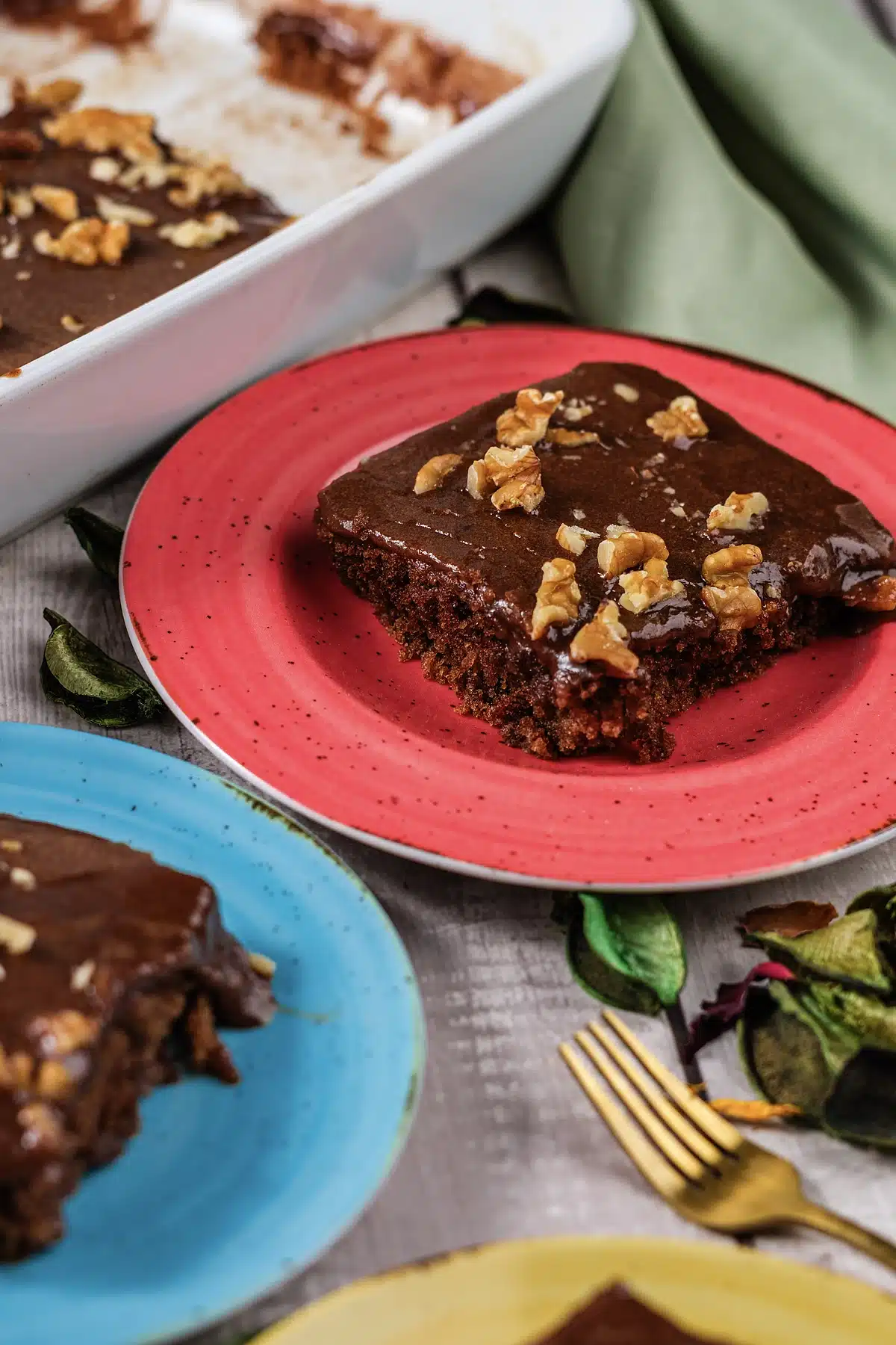 Texas sheet cake squares on red and blue plates beside the pan