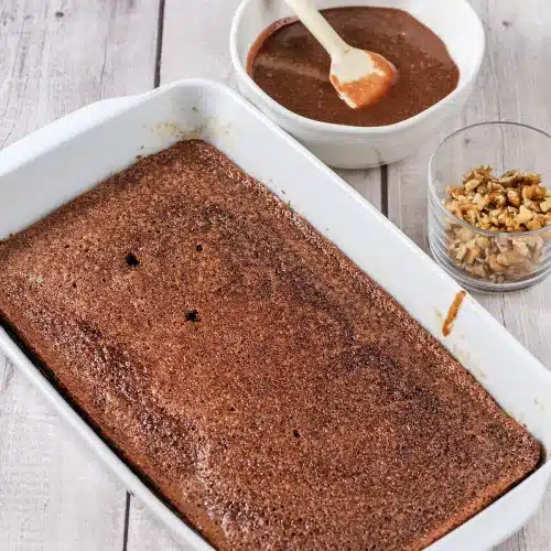 The baked cake in its dish with the icing and chopped nuts standing by