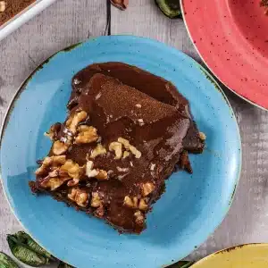 A single fudge-topped square on a blue plate with walnut pieces