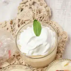A single glass of homemade vanilla pudding topped with whipped cream and a mint leaf
