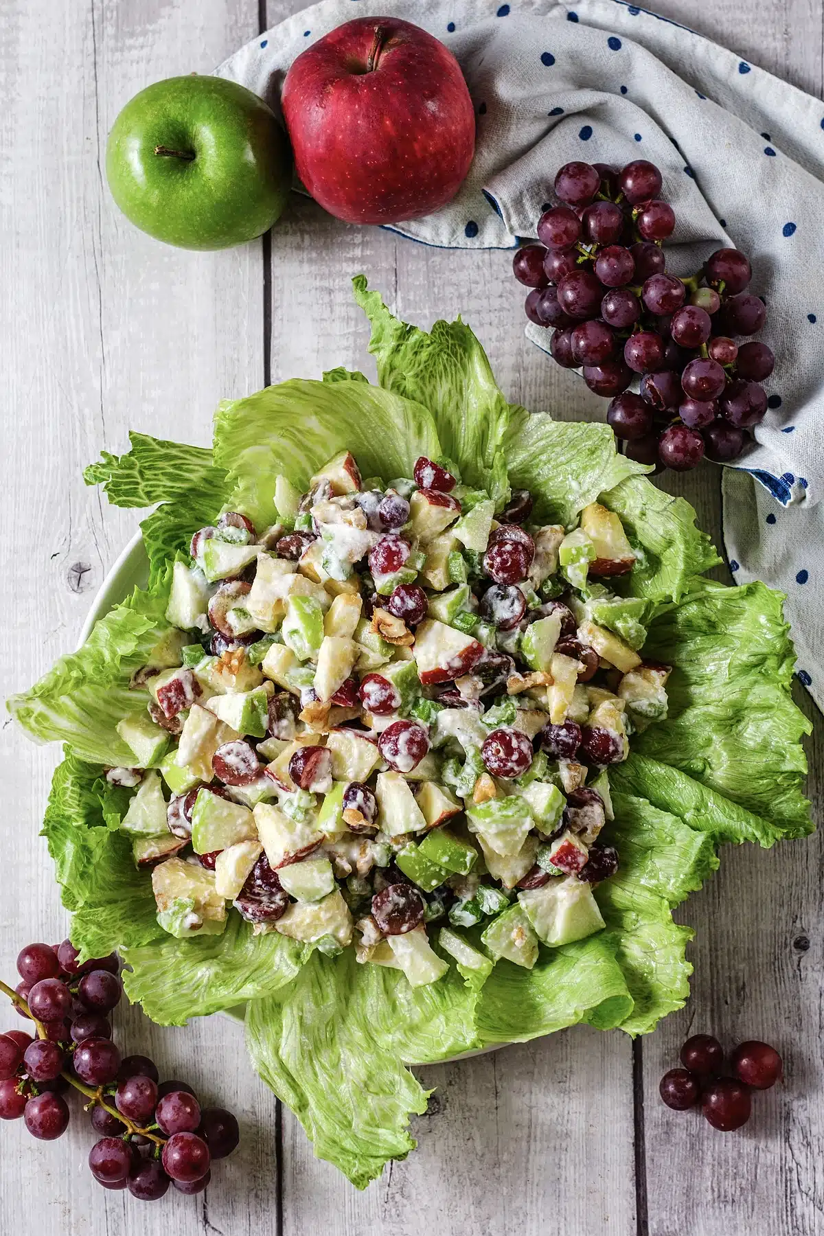 Classic Waldorf salad on lettuce with whole apples and a bunch of grapes behind