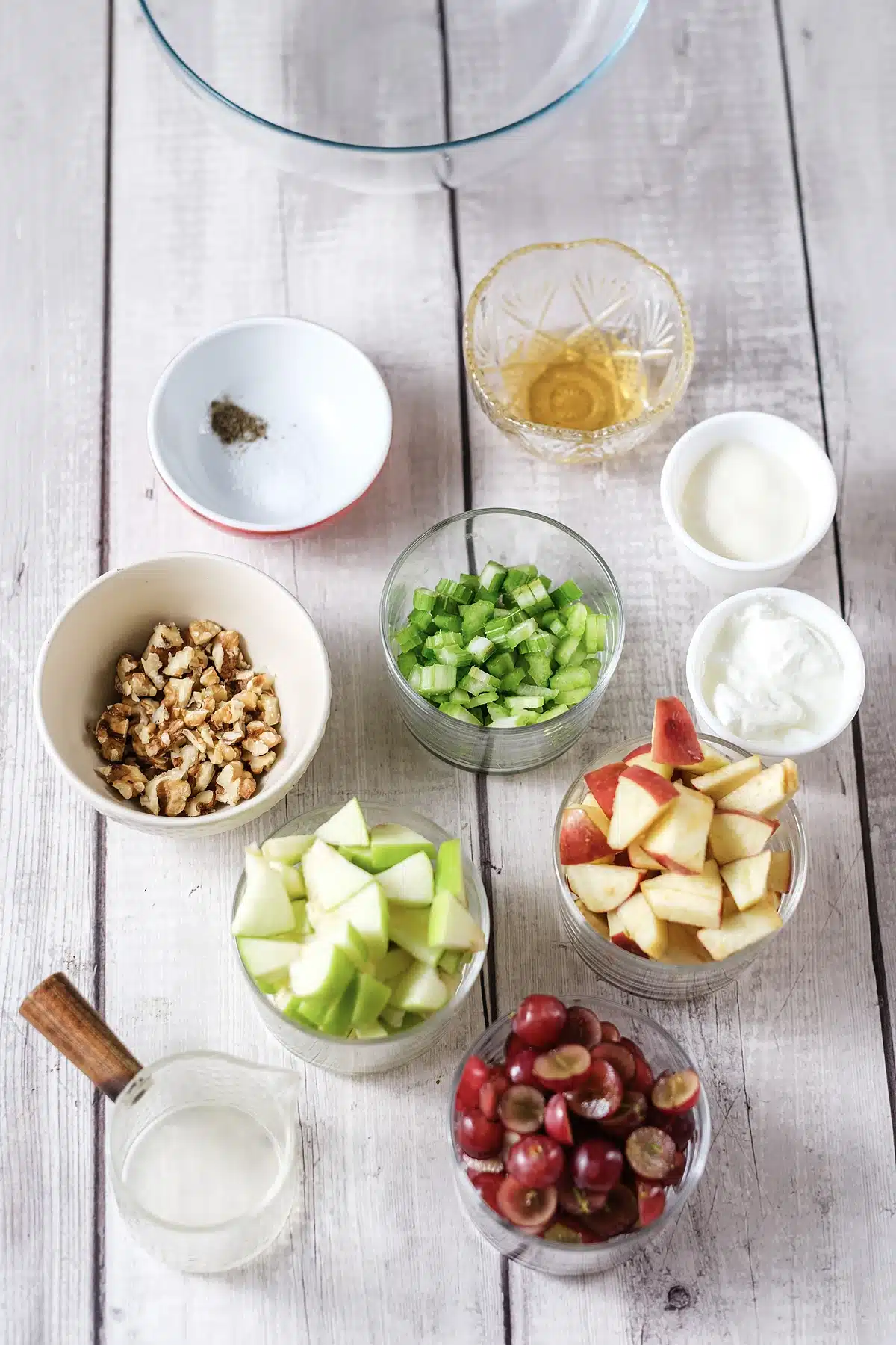 Diced apples, halved grapes, sliced celery, walnuts, mayonnaise and sour cream in bowls