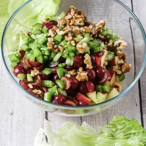 Grapes, celery and walnuts layered over the apple in a glass bowl