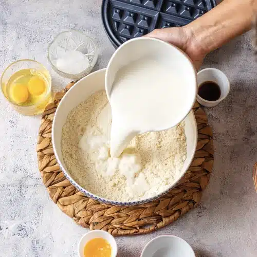 Milk poured from a white jug into a bowl of Bisquick mix