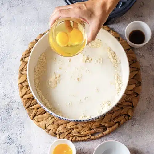 Two eggs tipped from a glass into the bowl of mix and milk
