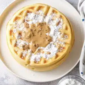 A single serving of Bisquick waffles with powdered sugar and peanut butter drizzle on a white plate