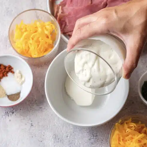 Sour cream spooned from a glass bowl into a white bowl of dressing