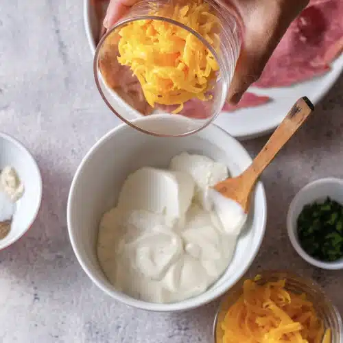 Shredded cheddar tipped from a glass into the bowl of sour cream and dressing