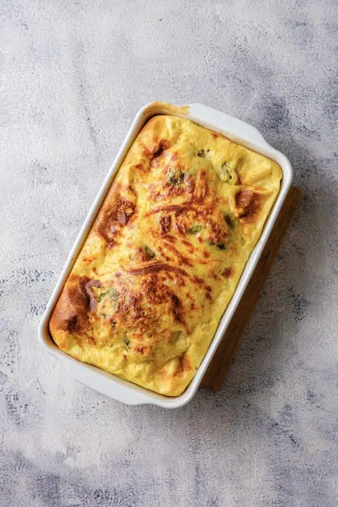 Chile relleno casserole baked golden in a white loaf-style dish on a wooden board, seen from directly above