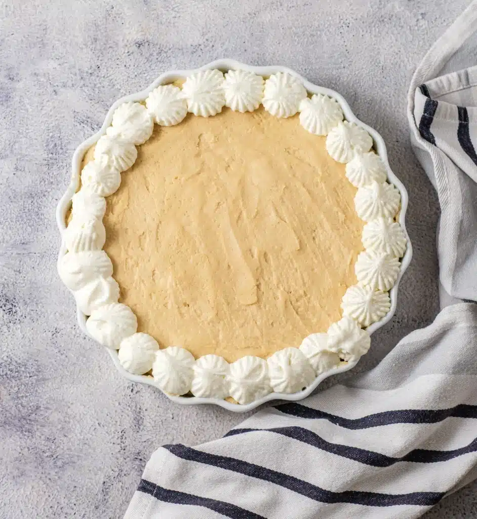 Dolly Parton's peanut butter pie in a fluted white dish with a piped whipped topping border, seen from above on a striped towel
