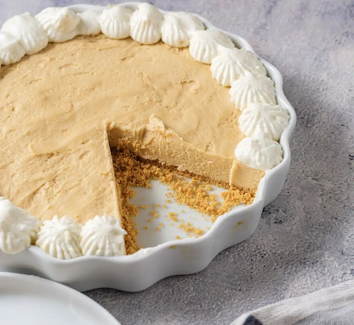 The cut dessert in a fluted white dish showing the graham crust, with a piped cream border and one wedge removed
