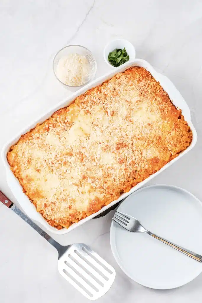 Olive Garden five cheese ziti al forno in a white baking dish, seen from directly above, with a plate and spatula beside it