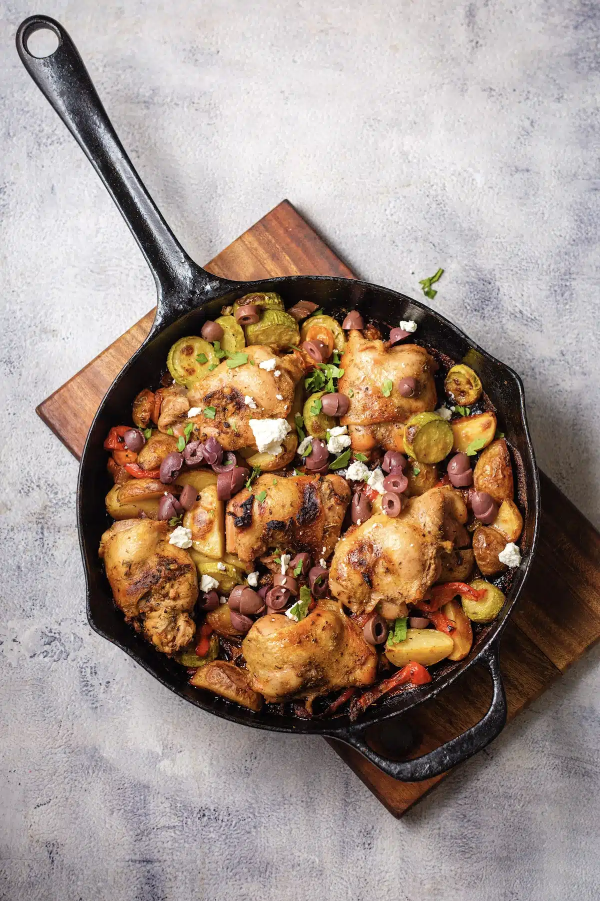 Greek sheet pan chicken in a cast-iron skillet with feta, olives and parsley on top, seen from directly above