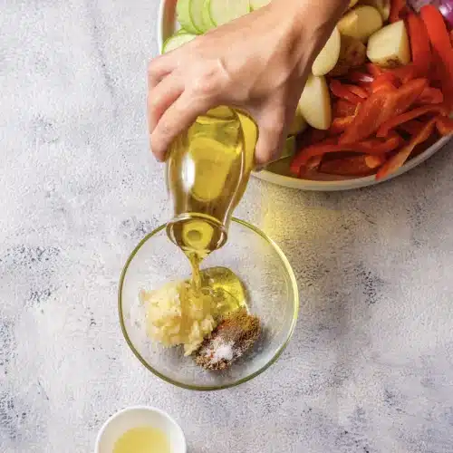 Olive oil poured from a bottle into a glass bowl of minced garlic and spices