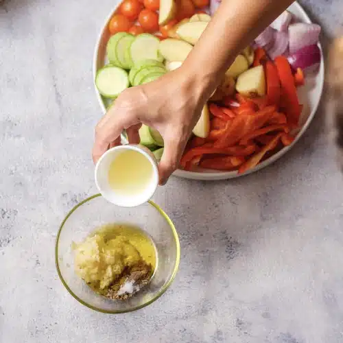 Lemon juice poured from a small cup into the bowl of oil, garlic and spices