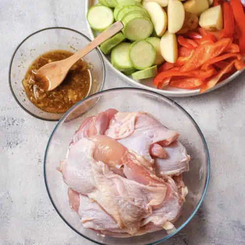 The whisked marinade in a small bowl beside a glass bowl of raw boneless thighs