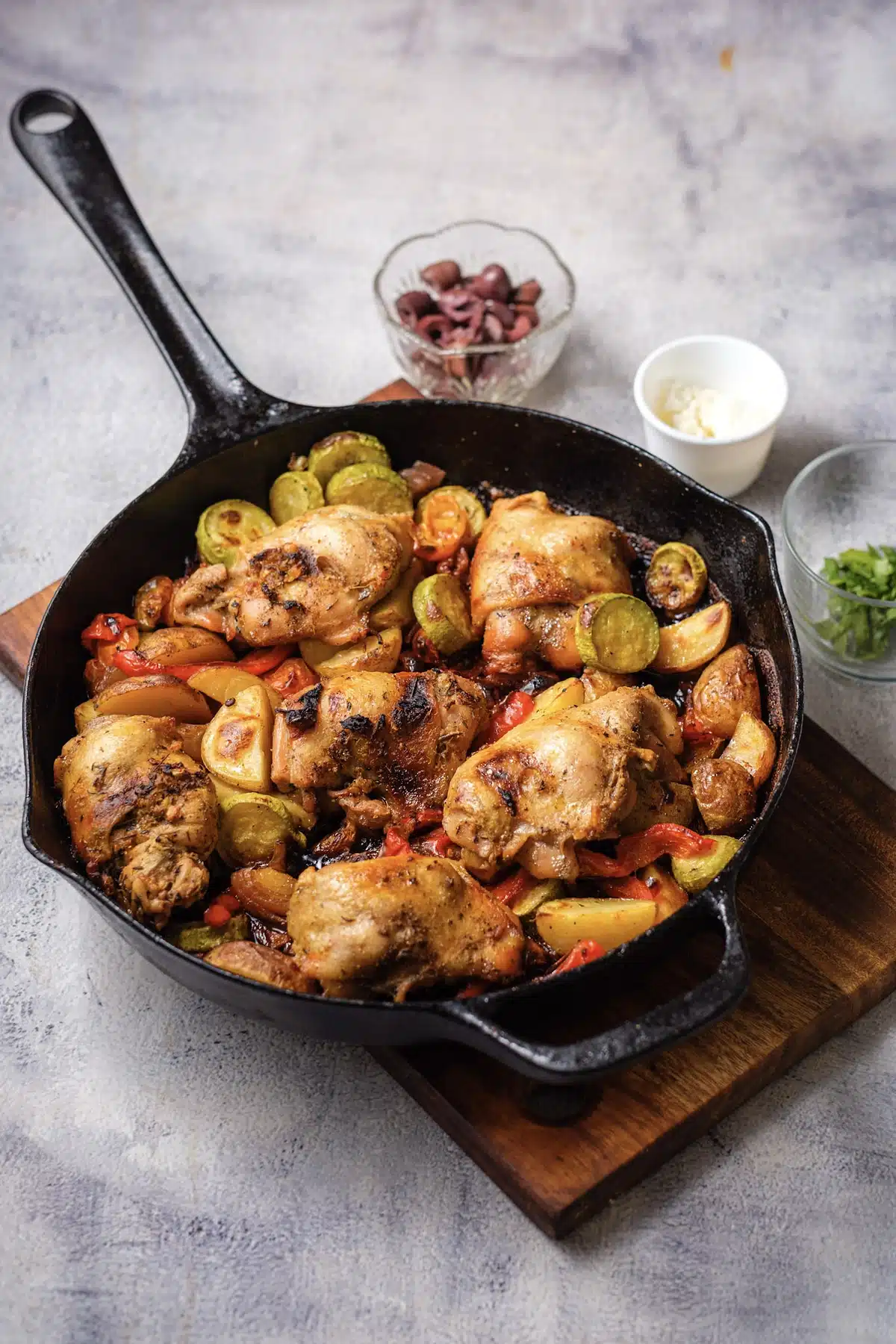 The finished skillet of roasted thighs, potato wedges, zucchini and peppers before the toppings go on, with small bowls of olives, feta and parsley