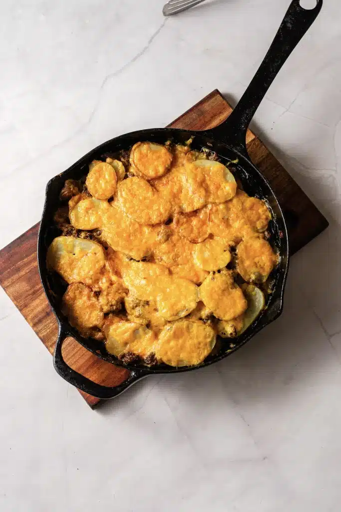 Hamburger potato casserole in a cast-iron skillet on a wooden board, seen from directly above