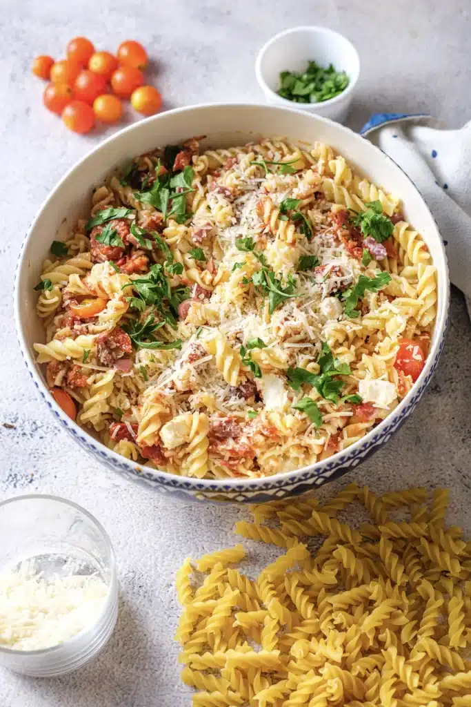 Ina Garten pasta salad in a white bowl with cherry tomatoes, parsley and grated Parmesan beside it, seen from directly above