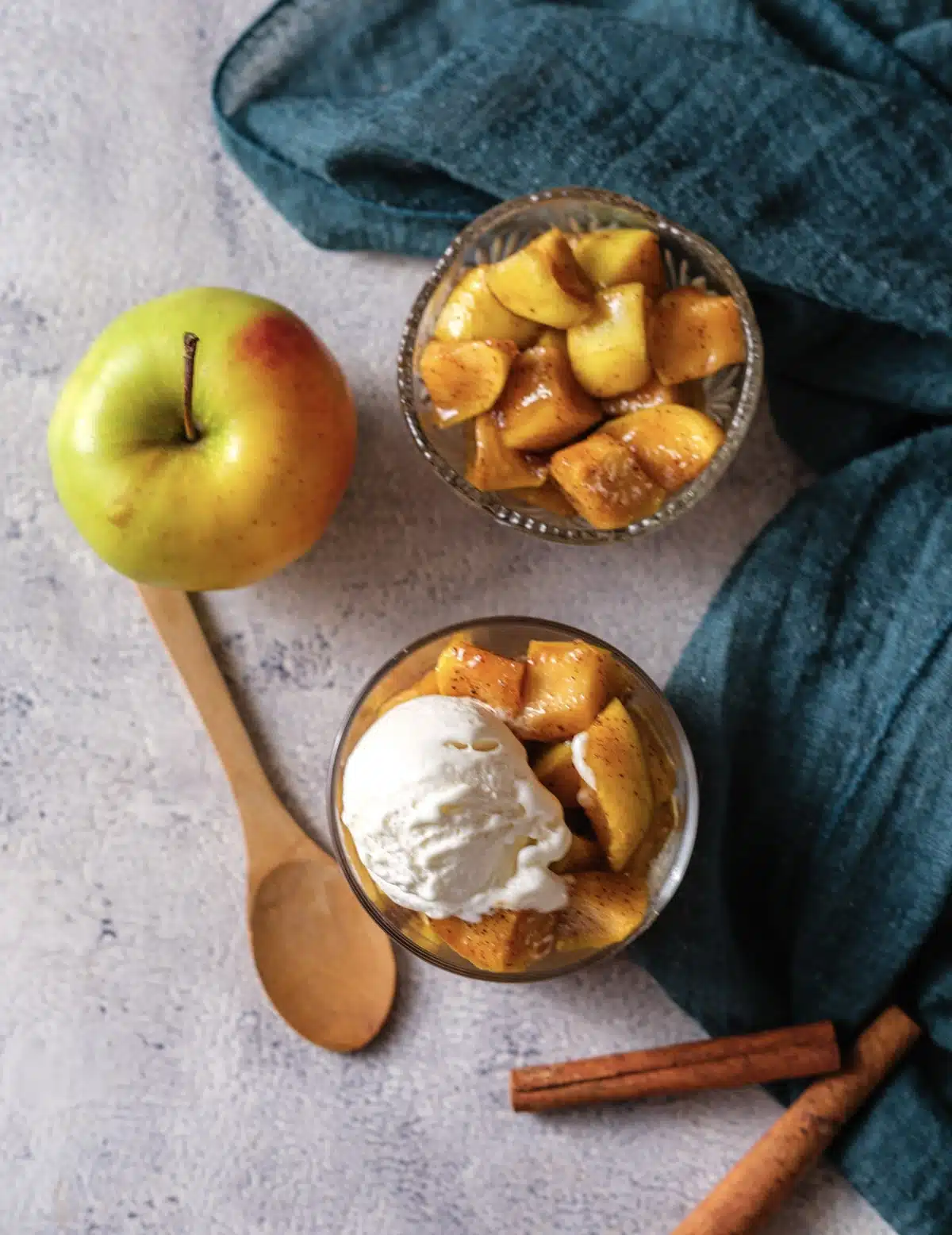 A close view of microwave baked apples in a glass with a scoop of vanilla ice cream melting over them and a whole apple behind