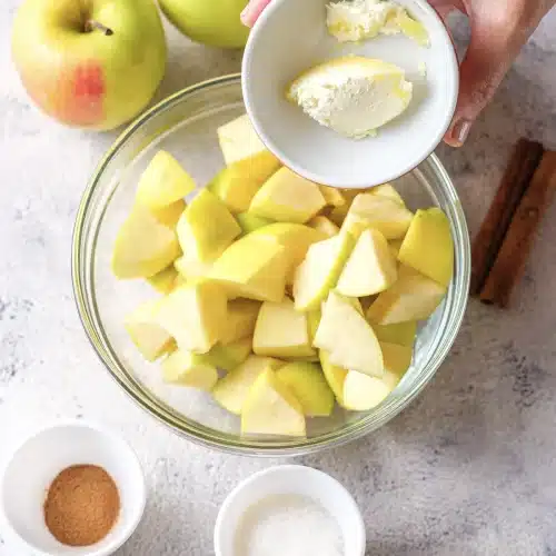 Butter tipped from a small bowl onto a glass bowl of raw fruit chunks
