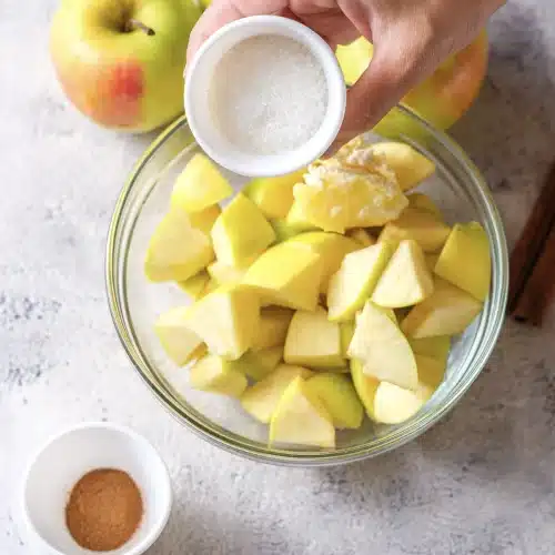 Sugar poured from a small white bowl over the fruit chunks and butter
