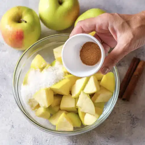 Ground spice sprinkled from a small bowl over the sugared fruit chunks
