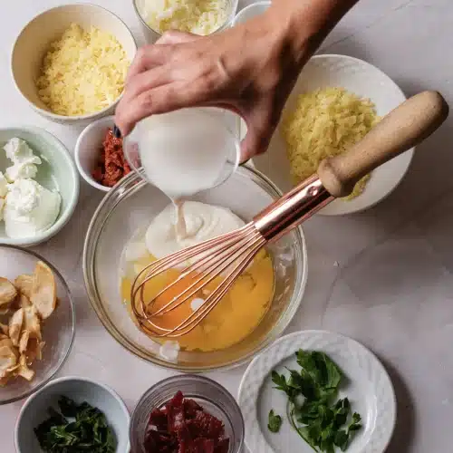 Milk poured into the bowl of eggs and cream