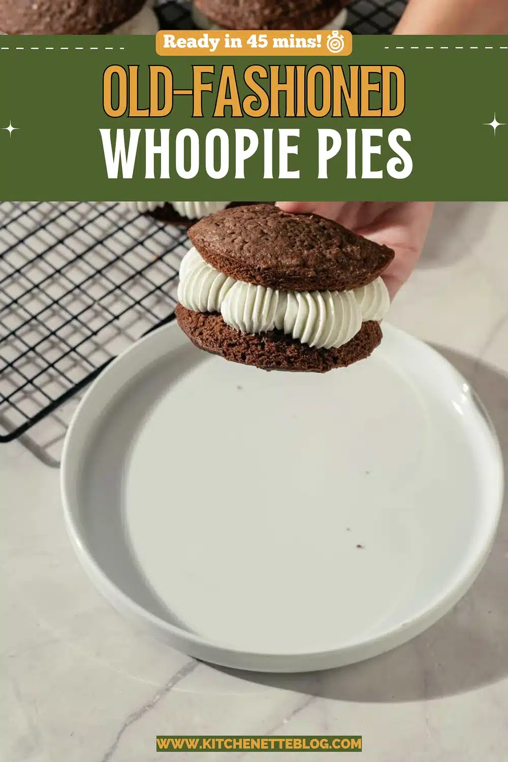 A hand placing the top chocolate cake on a cream-filled sandwich above a white plate