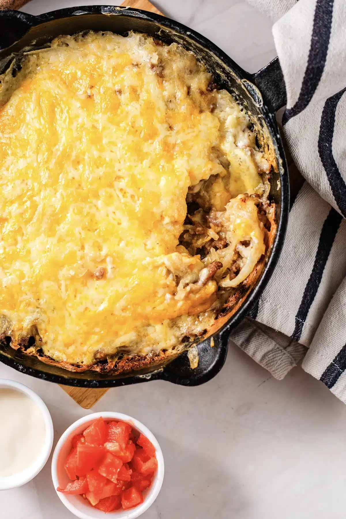 Close view of the taco hashbrown casserole with a corner scooped out, showing the shredded potato and beef under the cheese