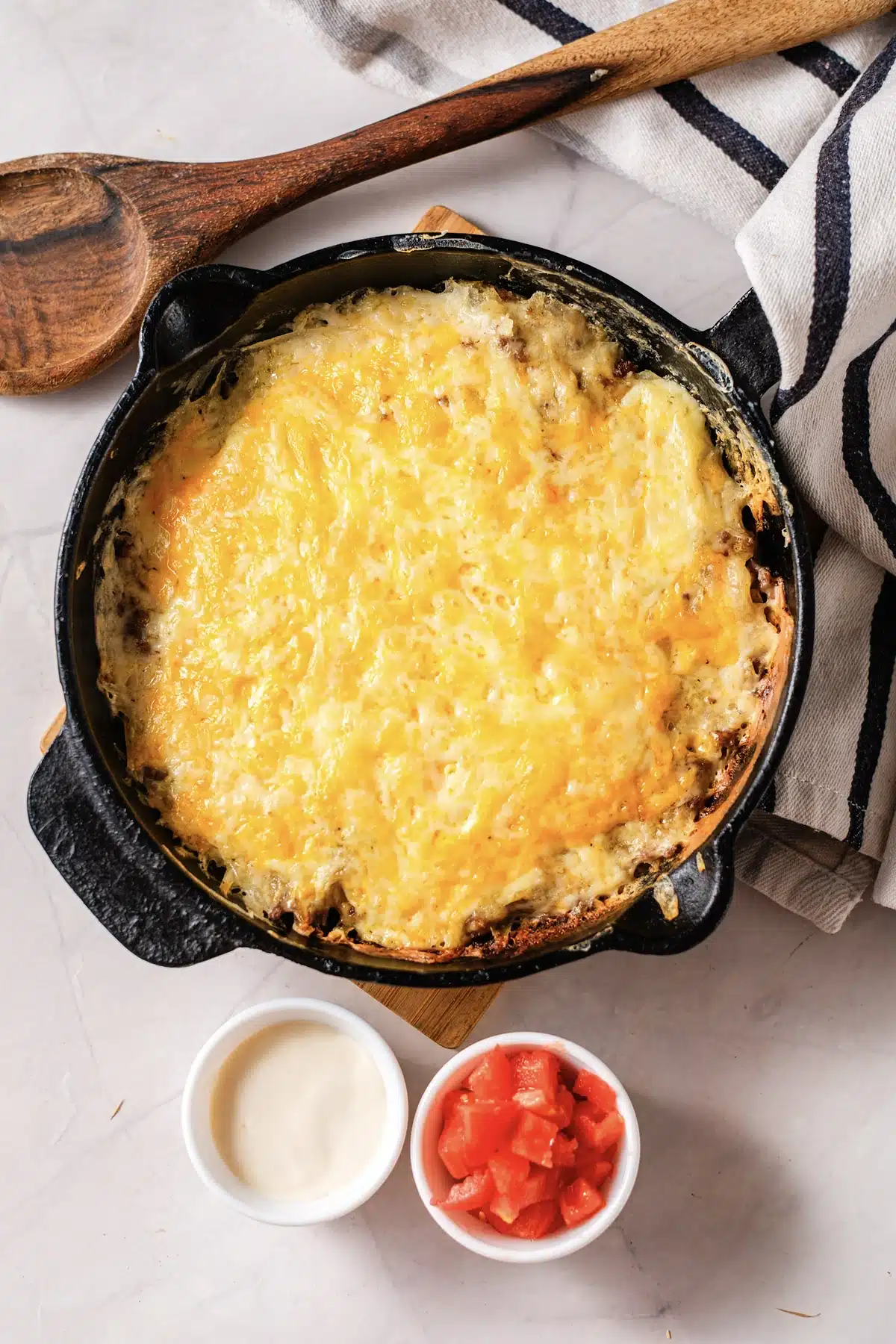 Taco hashbrown casserole in a cast-iron skillet with a scoop taken out, a wooden spoon and a striped towel beside it